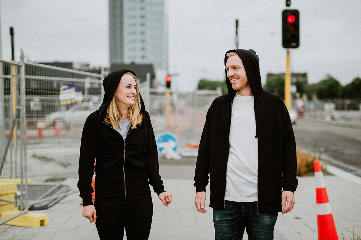 Two people standing side by side wearing fair trade organic cotton zippered black hoodies