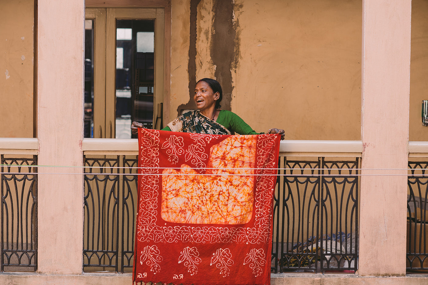 A smiling woman standing on a courtyard balcony hanging a sari on a washing line to dry.