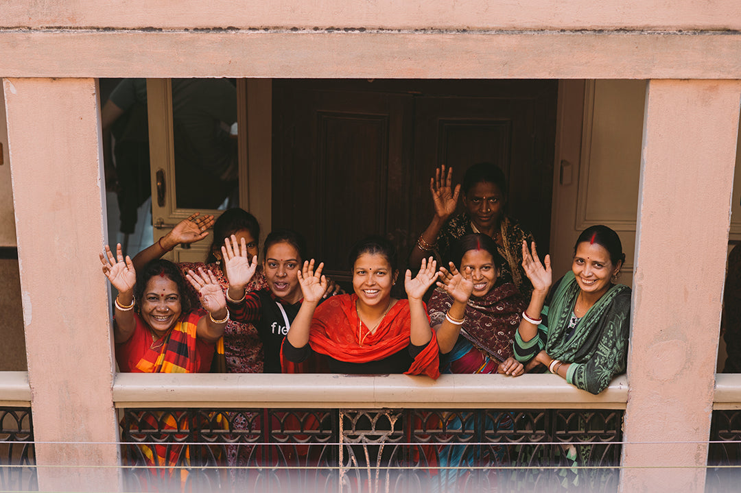 A group of Joyya staff woman standing on a balcony waving upward at the camera. 