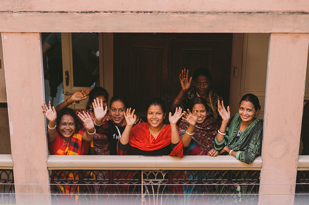 A group of Joyya staff woman standing on a balcony waving upward at the camera.