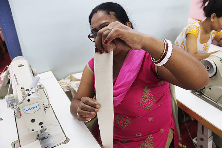 Two hands holding a folded piece of cotton for a handle on a fair trade organic Joyya tote bag. 