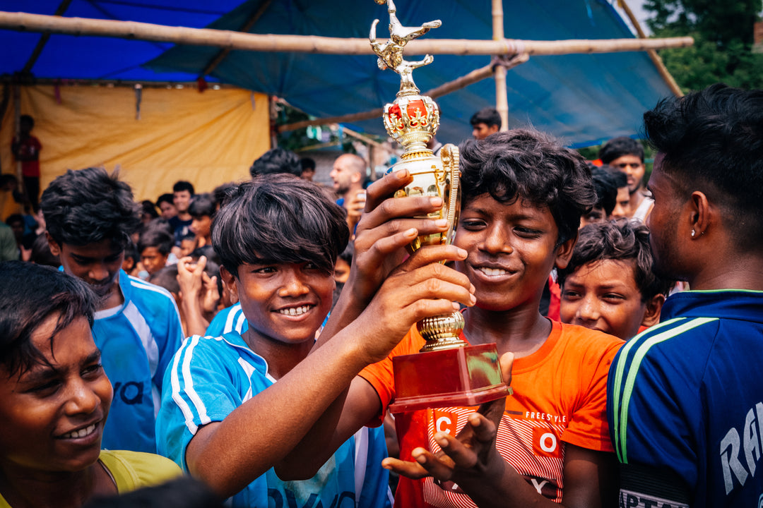 A group of young boys with two in the centre holding up a trophy after playing sports together. 