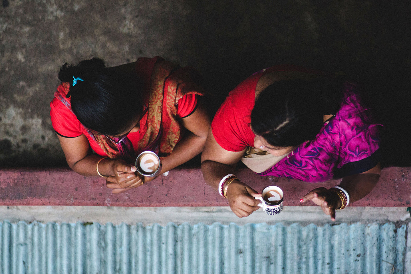 Look down from above at the tops of two women standing on a balcony drinking chia out of a mug in a Kolkata India 