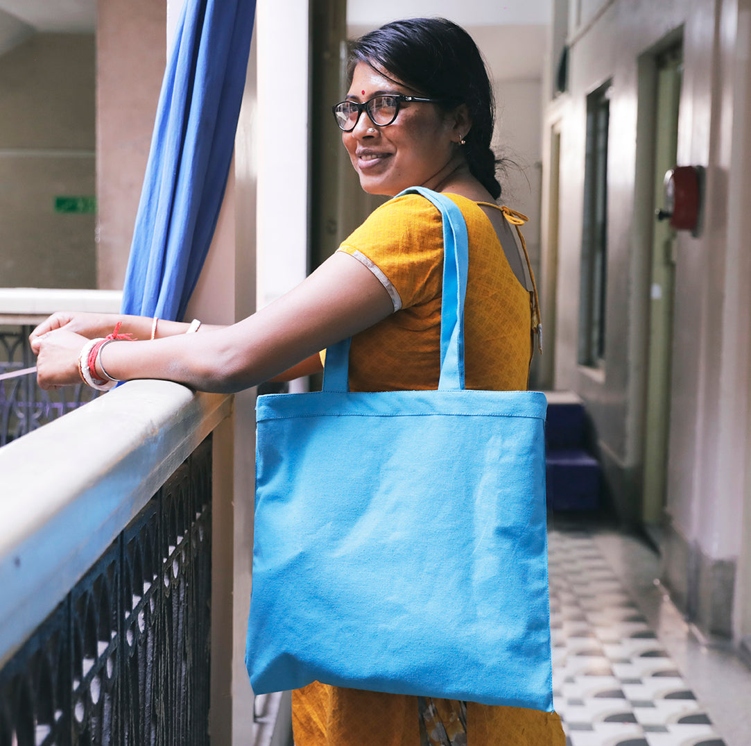 Joyya Staff woman holds a handmade cotton canvas blue tote bag in hallway