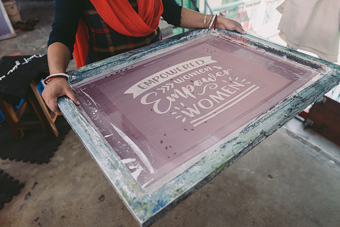 a woman holding a t-shirt screen printing tray with a design etched into the surface. The design reads Empowered Women Empower Women