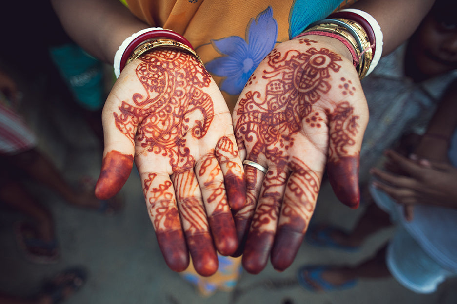 Looking downward at the open palms of a womans hands. The hands have been painted in an ornate fashion using henna. 