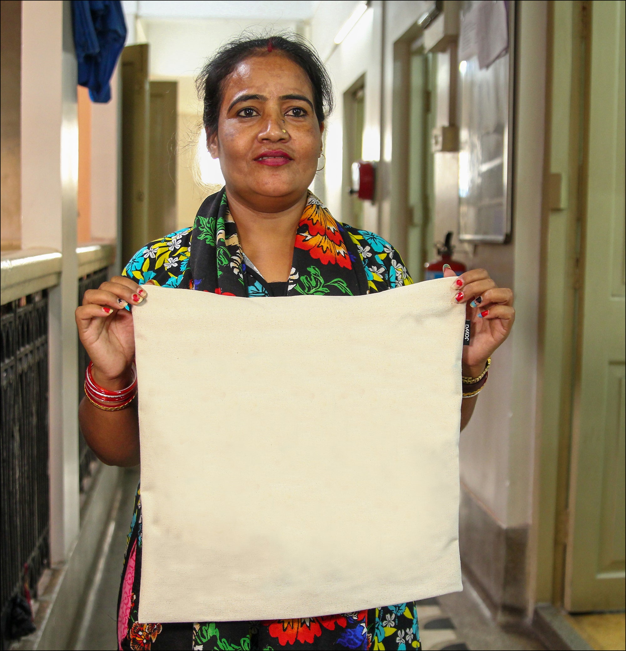 A Joyya staff woman is holding a blank natural color cotton canvas tote bag from each corner showing it to the camera.