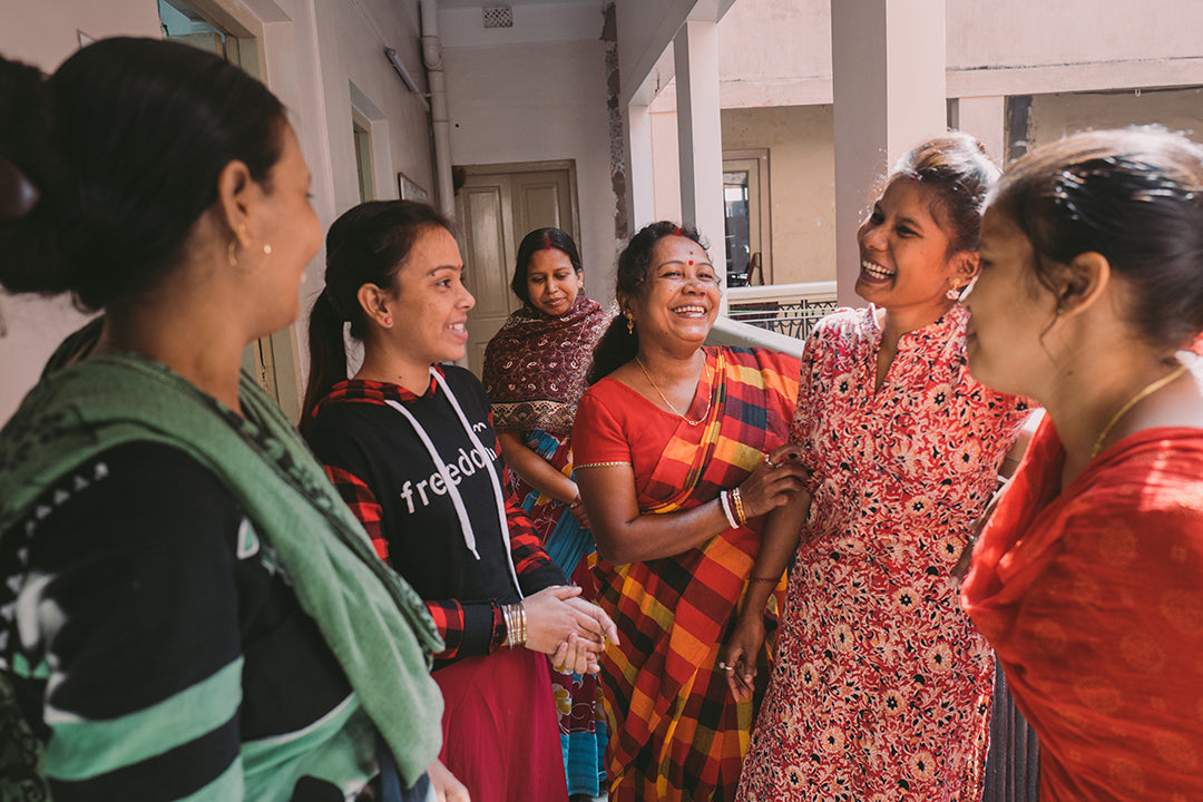 A group of 6 Joyya staff women gathered around talking and laughing in a hallway balcony. 