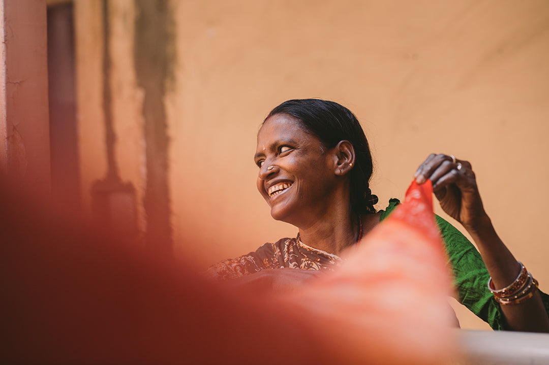 A female staff member of Joyya looking to the left with a large smile. She is holding a long piece of Sari fabric draping towards the camera.