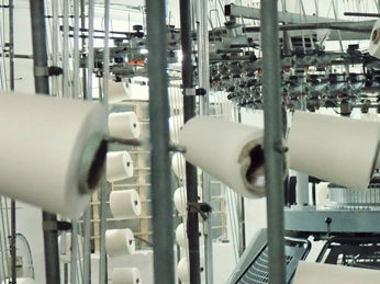 A close up image of many spools of cotton thread being feed into a large weaving machine for t-shirt cotton production.
